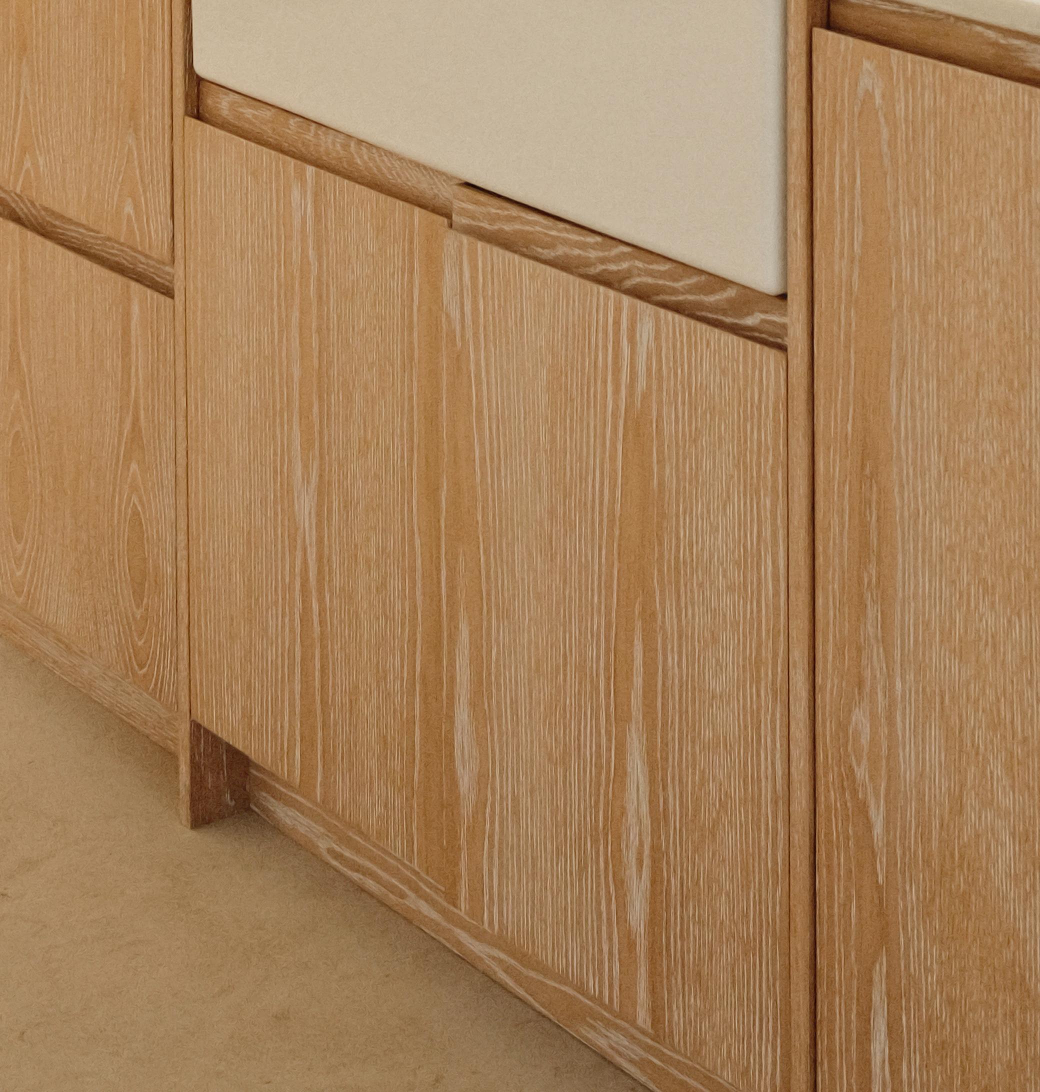 Light wood cabinets with a visible natural grain pattern and vertical paneling, set against a beige floor. The cabinet doors have no visible handles, giving a minimalist appearance.