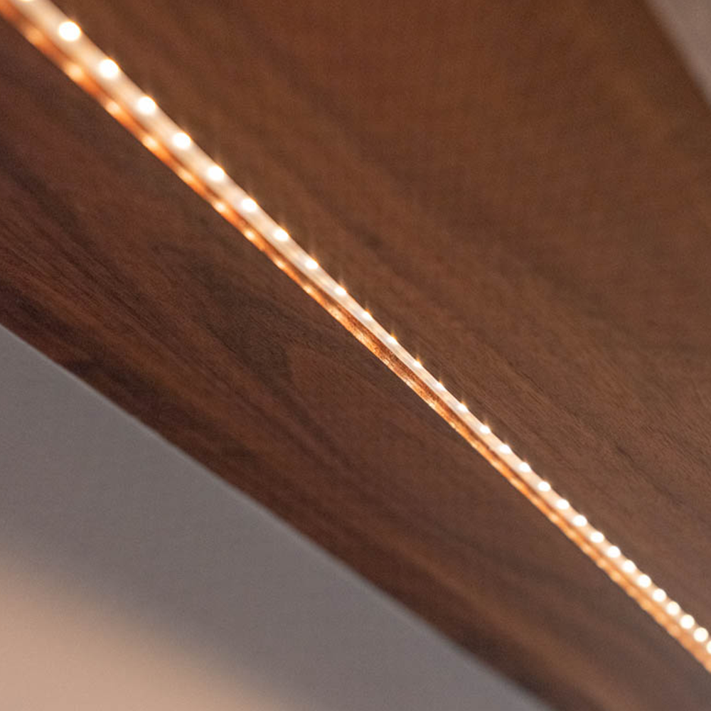 Close-up of a strip of warm white LED lights embedded along the edge of a wooden surface, creating a glowing line on the wood.