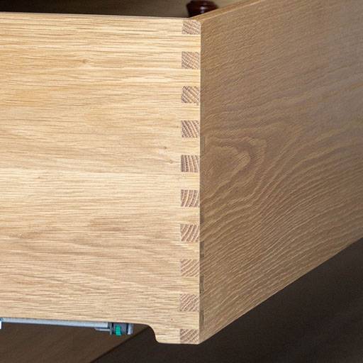 Close-up of a wooden drawer corner featuring interlocking dovetail joints, showcasing fine craftsmanship and wood grain detail.