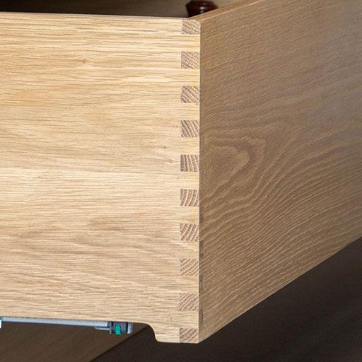 Close-up of a wooden drawer corner featuring interlocking dovetail joints, showcasing fine craftsmanship and wood grain detail.