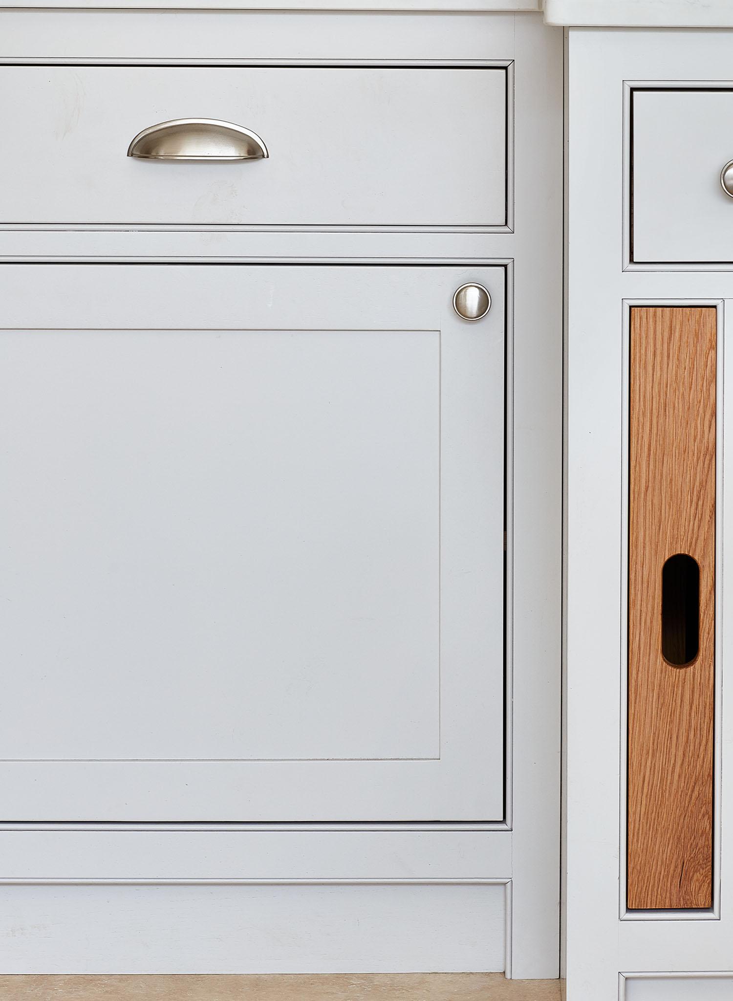 Close-up of kitchen cabinets showcasing a combination of white and wood finishes. A silver handle is attached to the top drawer, while the lower cabinet door features a round silver knob and the adjacent panel displays a vertical wood accent with a black rectangular cutout.
