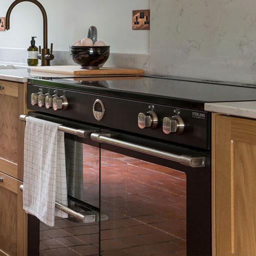 A modern black and stainless steel oven with a checkered towel hanging on the handle, set between wooden kitchen cabinets. A bowl of eggs and a soap dispenser sit on the countertop above