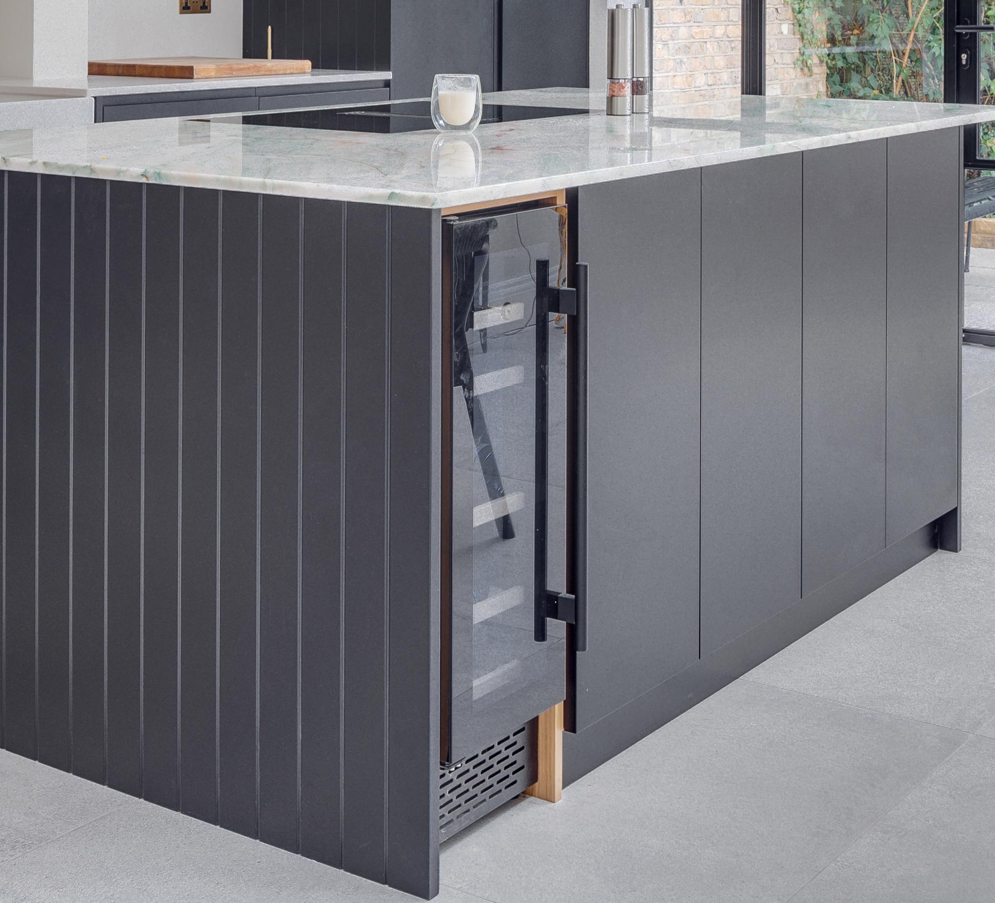 A modern kitchen island with a marble countertop features a built-in glass-front wine cooler with the door partially open, revealing shelves inside.