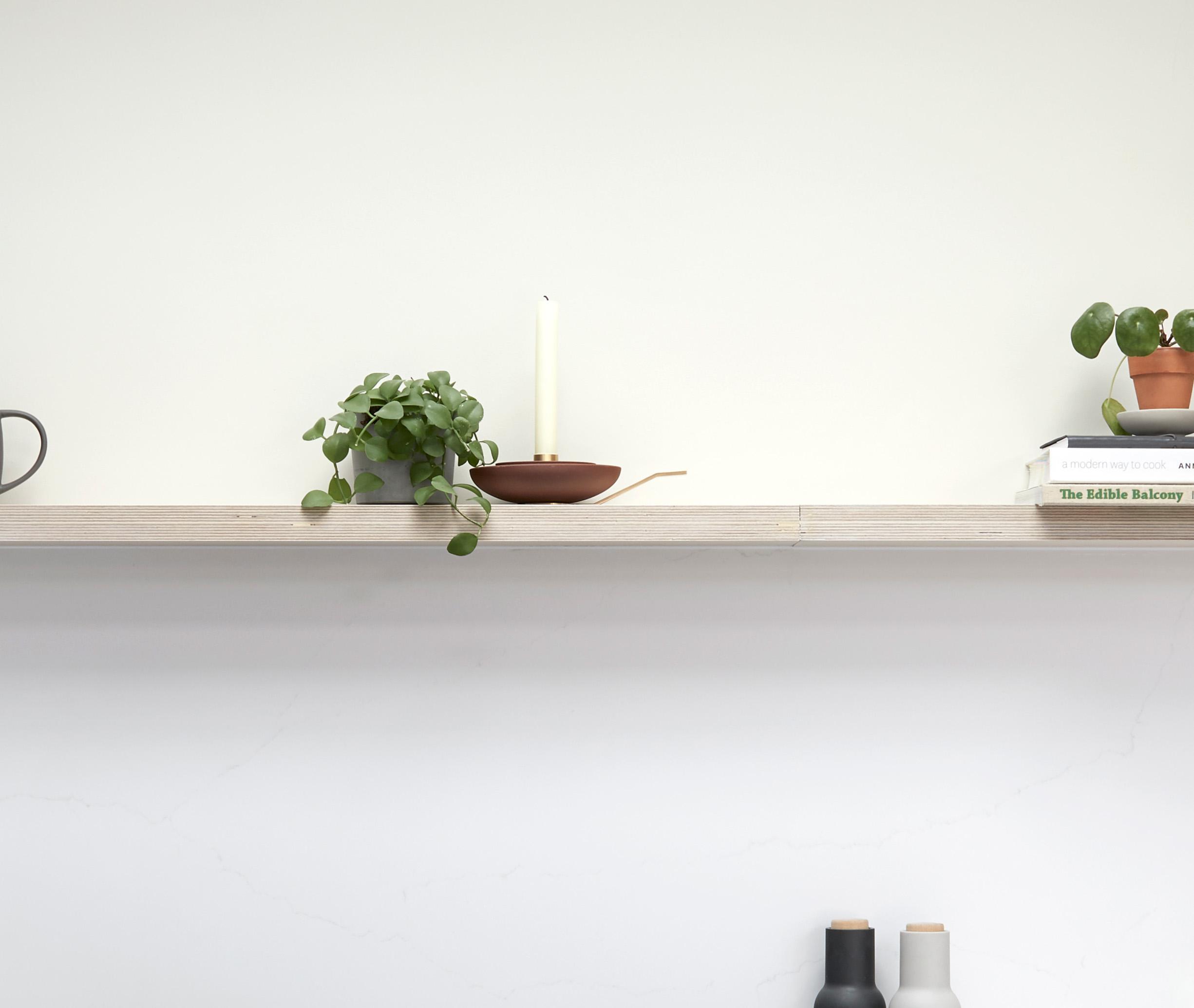 A minimal wooden shelf with a potted plant, a candle in a holder, and stacked books with another small plant on top. The background is plain white, giving a clean and simple look.