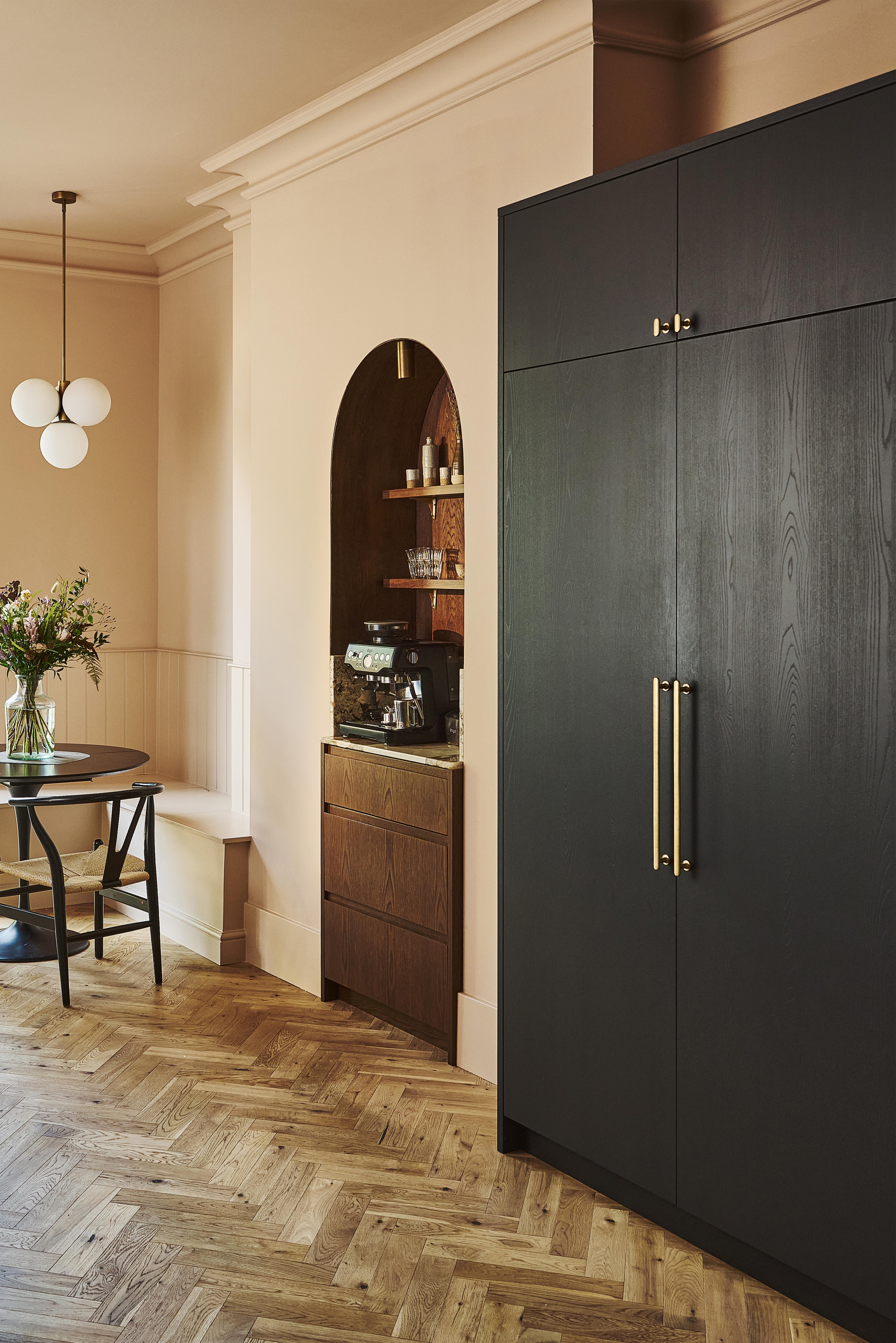A modern kitchen with wooden cabinets, marble backsplash, a built-in oven, cookware on the stove, open shelves holding plates, bowls, framed art, and decorative items, lit by two gold pendant lights.