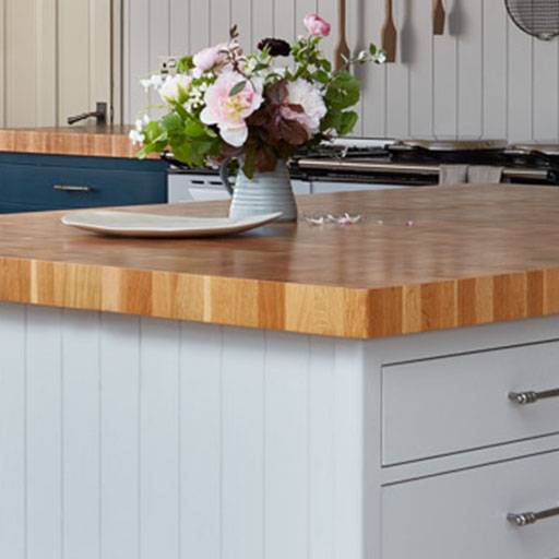 A light wood kitchen island countertop with a white vase of pink and white flowers and a rectangular plate on top; gray drawers and cabinets are visible below.