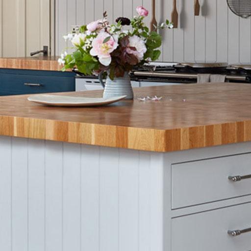 A light wood kitchen island countertop with a white vase of pink and white flowers and a rectangular plate on top; gray drawers and cabinets are visible below.