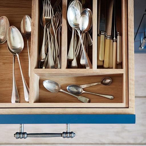 An open drawer with a wooden organizer holding assorted silverware, including spoons, forks, and knives with cream handles. Several spoons are scattered outside the compartments.