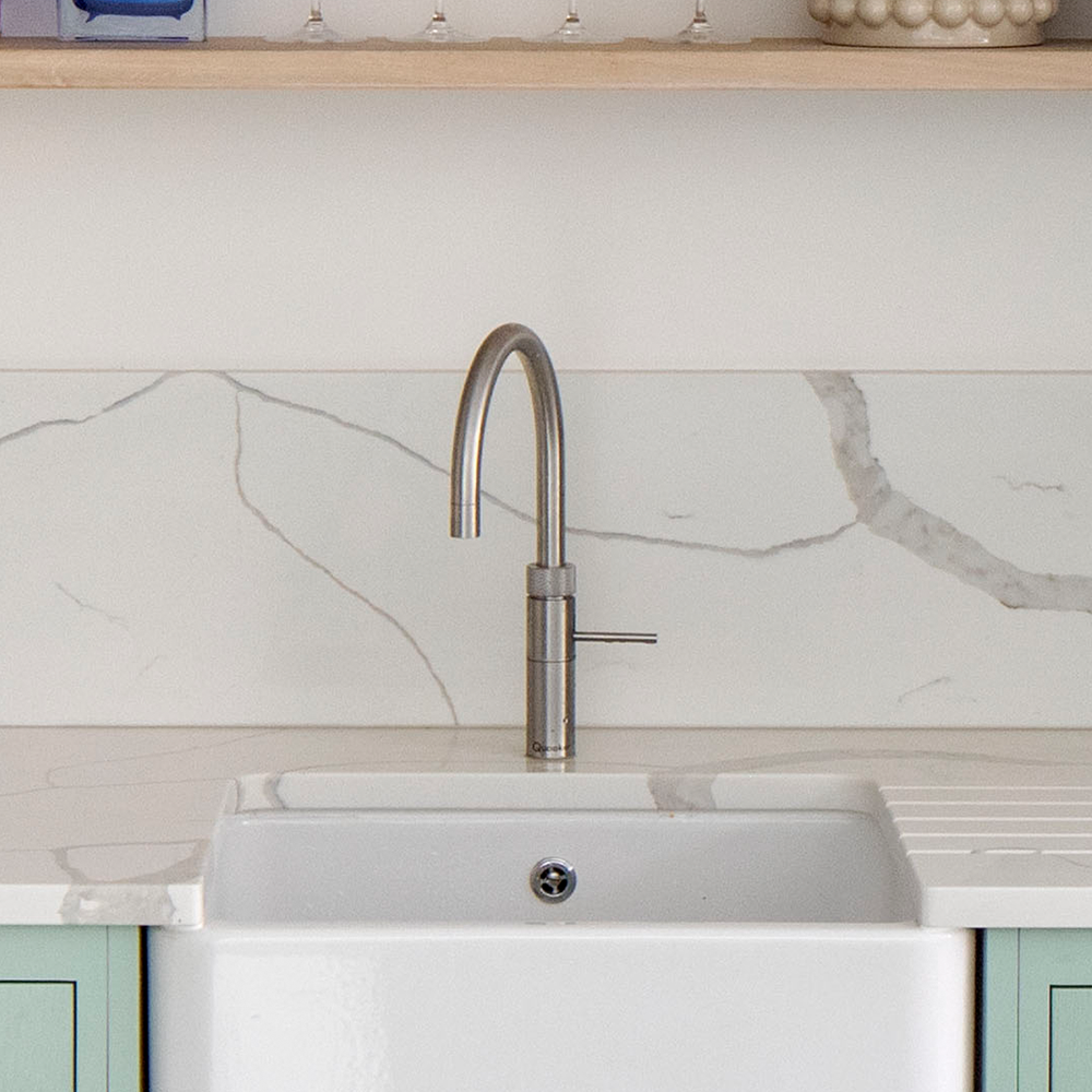 A modern kitchen sink with a sleek stainless steel faucet, set in a white countertop with a marble-patterned backsplash. Light green cabinets are partially visible below the sink.