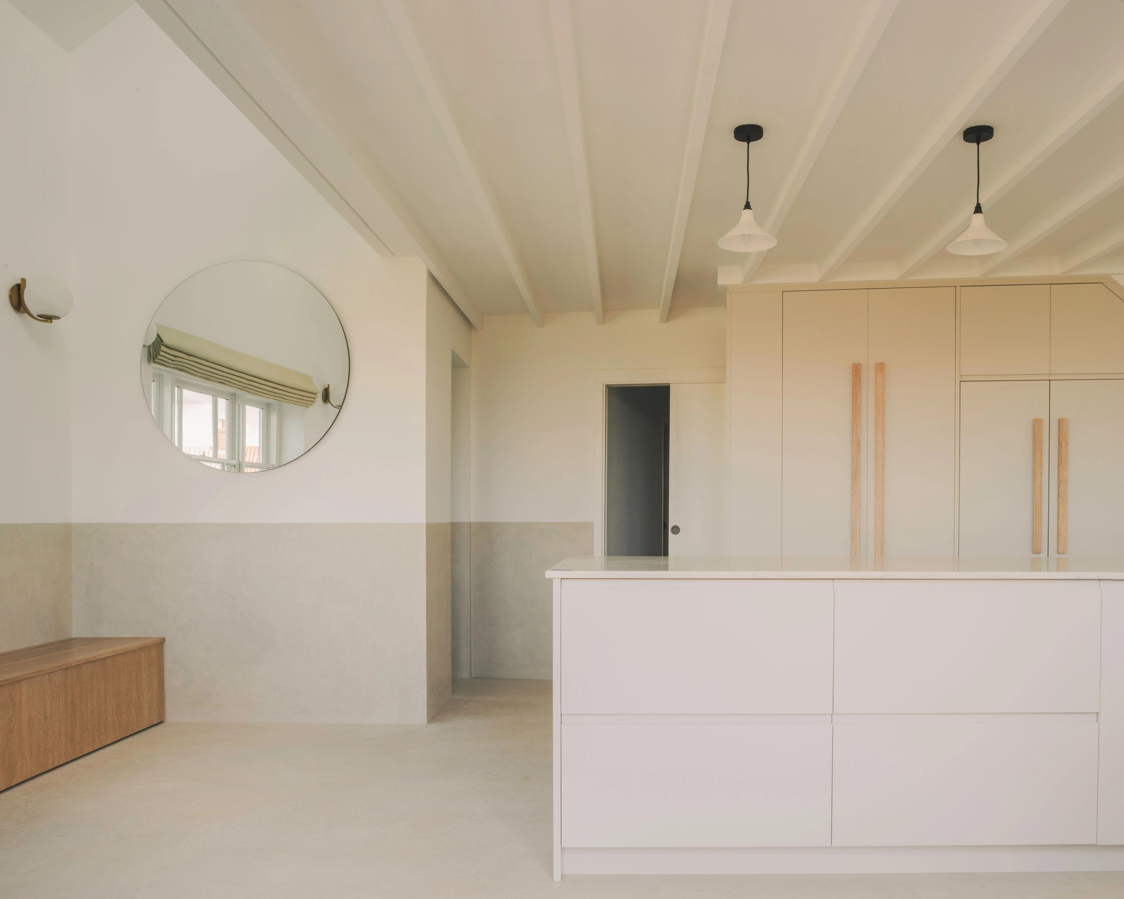 A modern kitchen with mustard-colored cabinets, a patterned backsplash, and a white countertop island with cooking stoves. Three pendant lights hang above the island, and there are shelves with decor items on the left.
