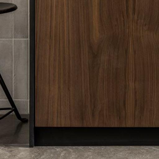 A close-up of a modern kitchen cabinet with a dark wood finish next to a black metal bar stool on a gray tiled floor and wall