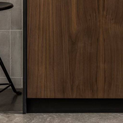 A close-up of a modern kitchen cabinet with a dark wood finish next to a black metal bar stool on a gray tiled floor and wall
