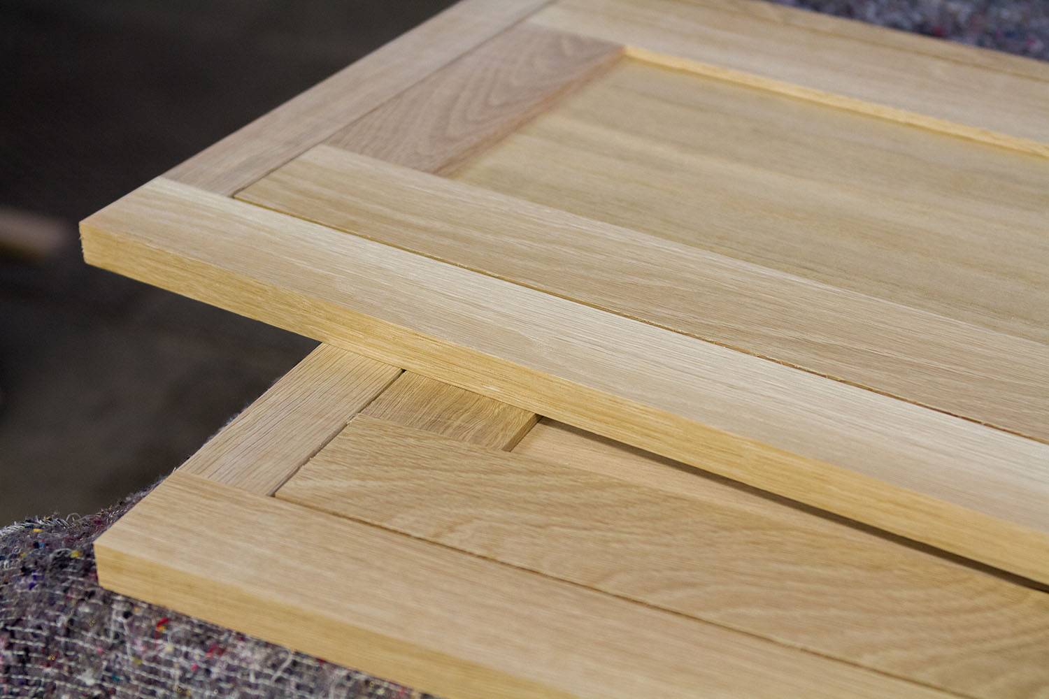 Two wooden cabinet doors with a natural finish are stacked on top of each other. The doors have a simple, flat panel design and are placed on a textured surface.