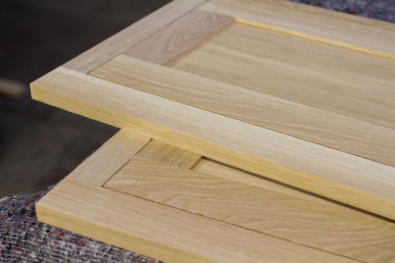 Two wooden cabinet doors with a natural finish are stacked on top of each other. The doors have a simple, flat panel design and are placed on a textured surface.