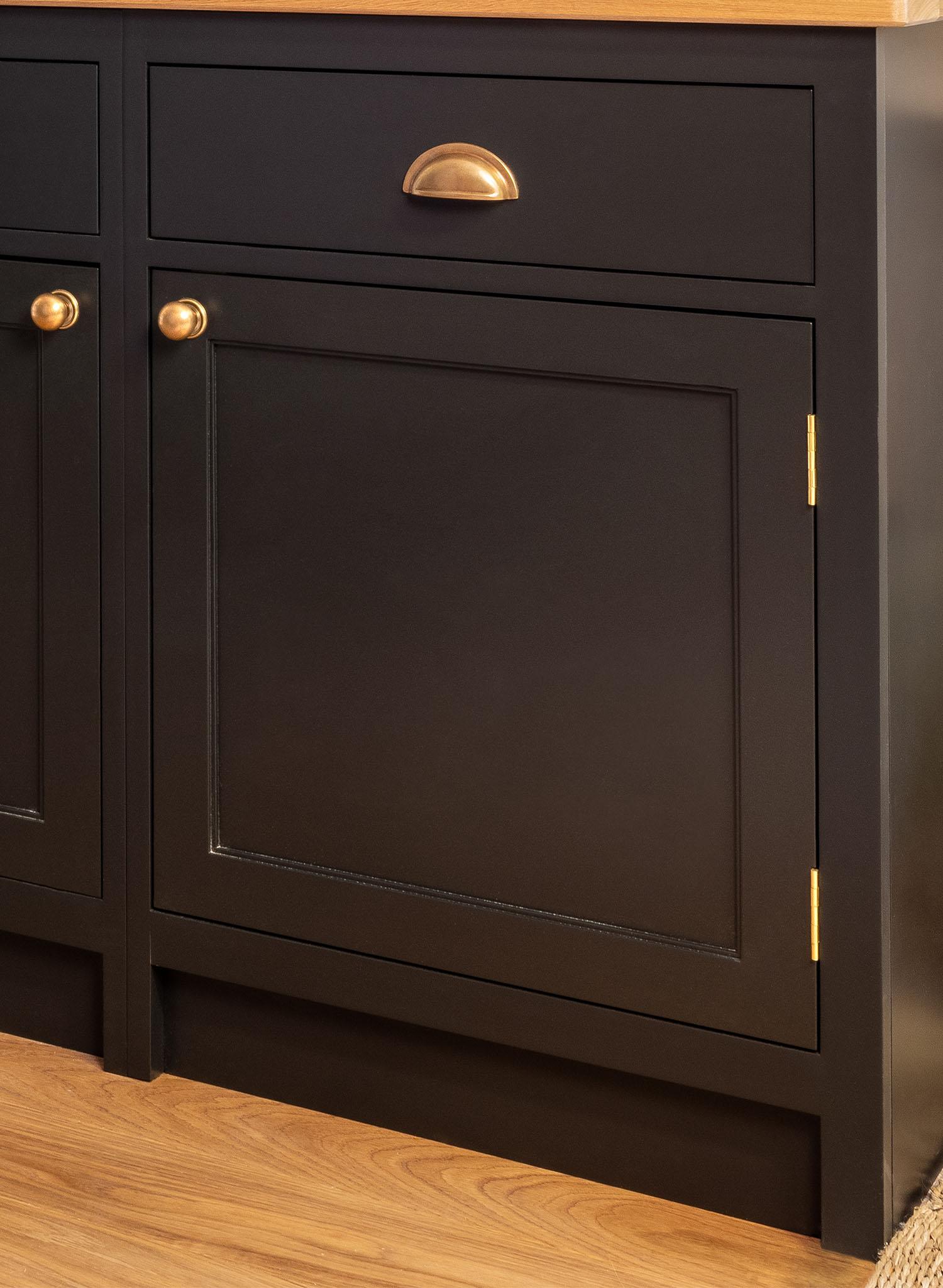 A close-up of dark-colored kitchen cabinets with gold handles and a wood countertop, set against a light wood floor.