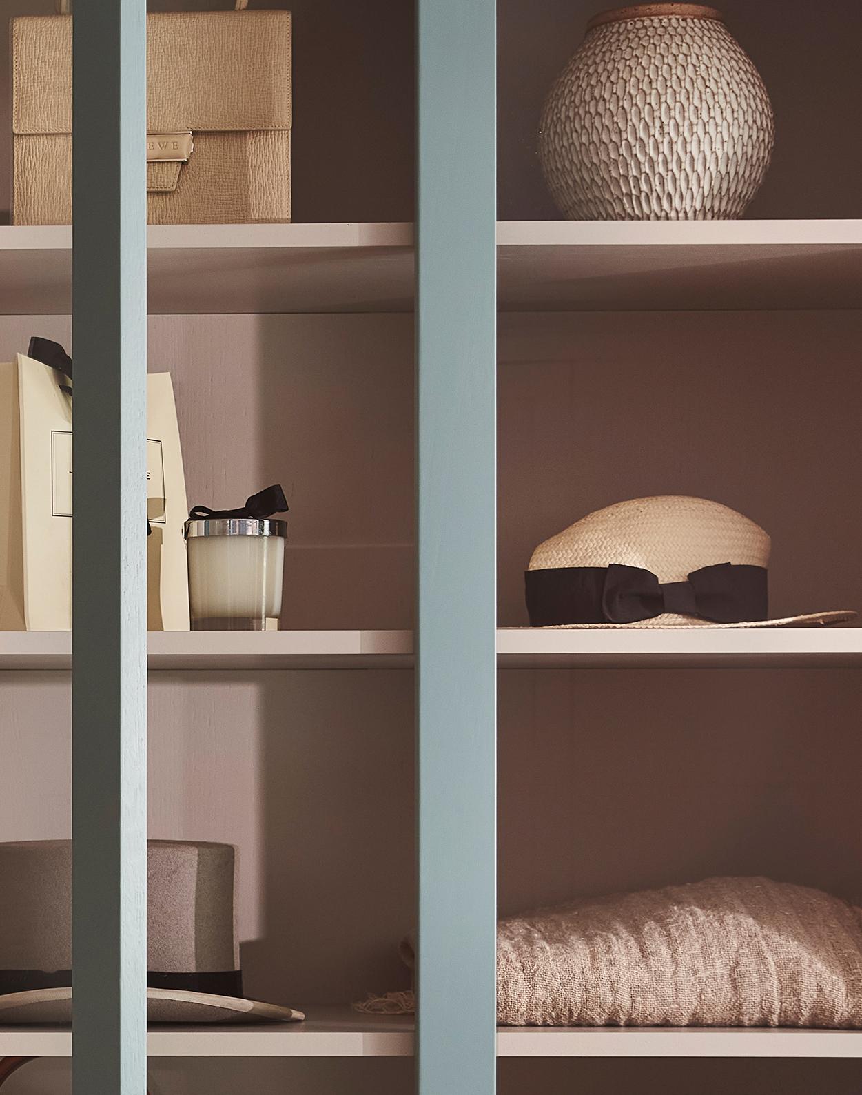 Shelves with decorative items including stacked boxes, a textured vase, a candle, a folded sweater, and hats, viewed partially through vertical blue slats