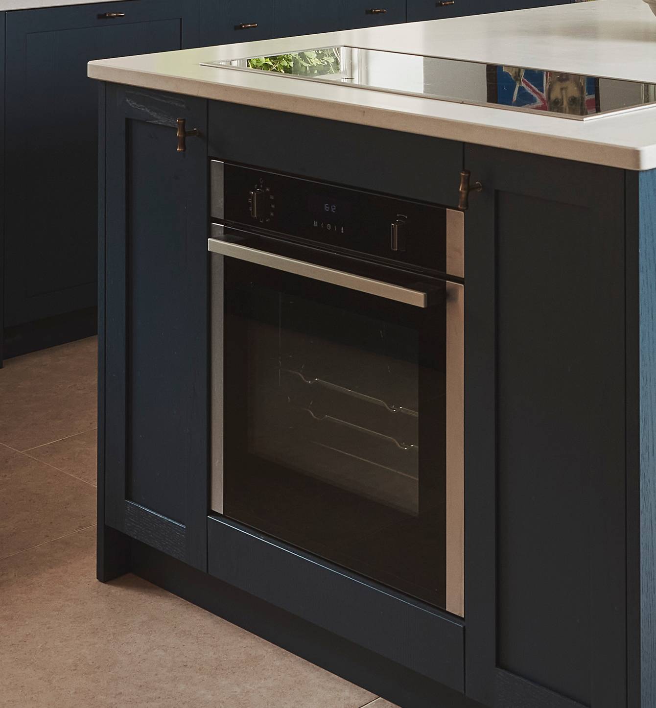 A modern built-in oven with a digital display and stainless steel handle is integrated into a dark blue kitchen island with a white countertop.