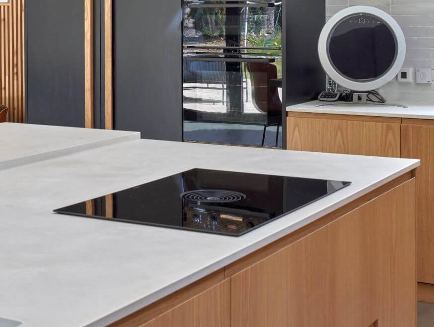 Modern kitchen with a sleek induction cooktop built into a light-colored countertop, wooden cabinets, and a double oven