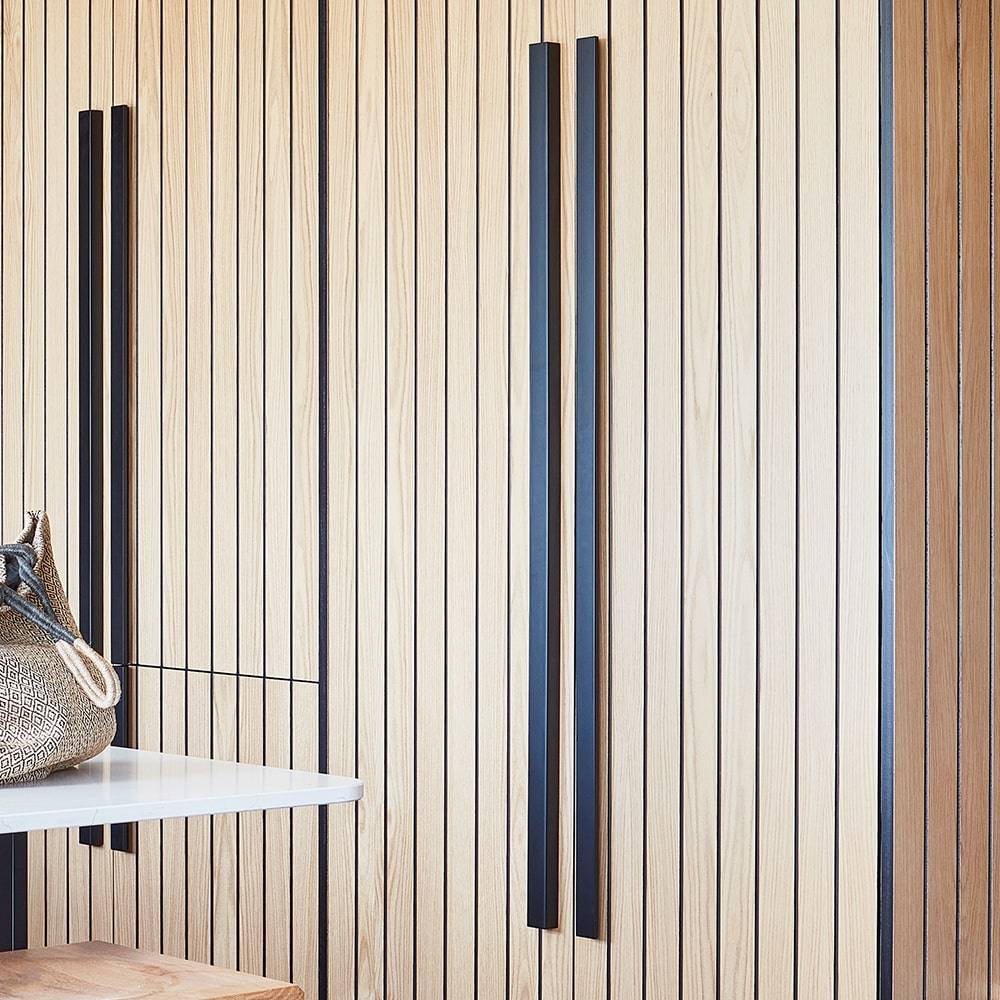 Vertical wooden panels with thin black lines cover a wall, featuring two tall black handles. A small corner of a white table and a woven bag are visible in the lower left corner.