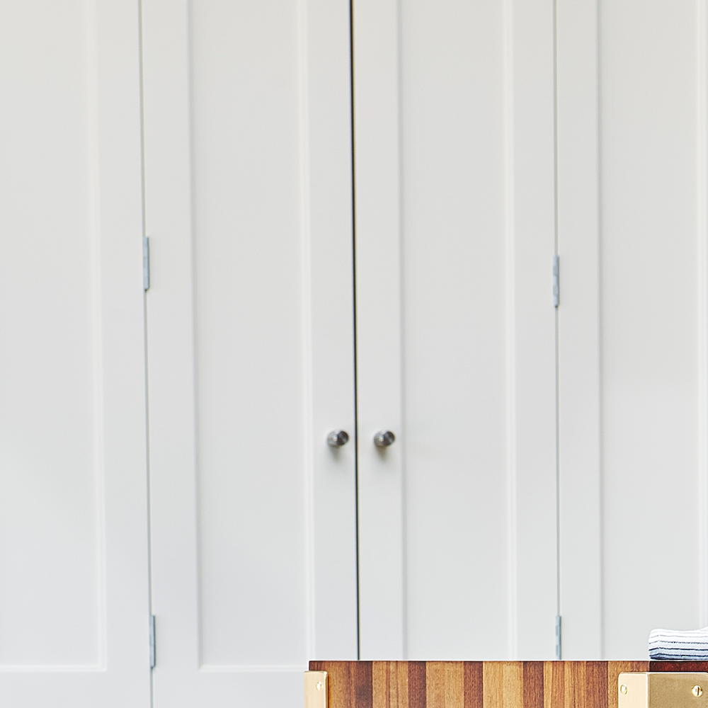 A pair of closed white double doors with silver handles, set against a plain wall. In the foreground, a wooden surface and a small stack of folded clothes are partially visible