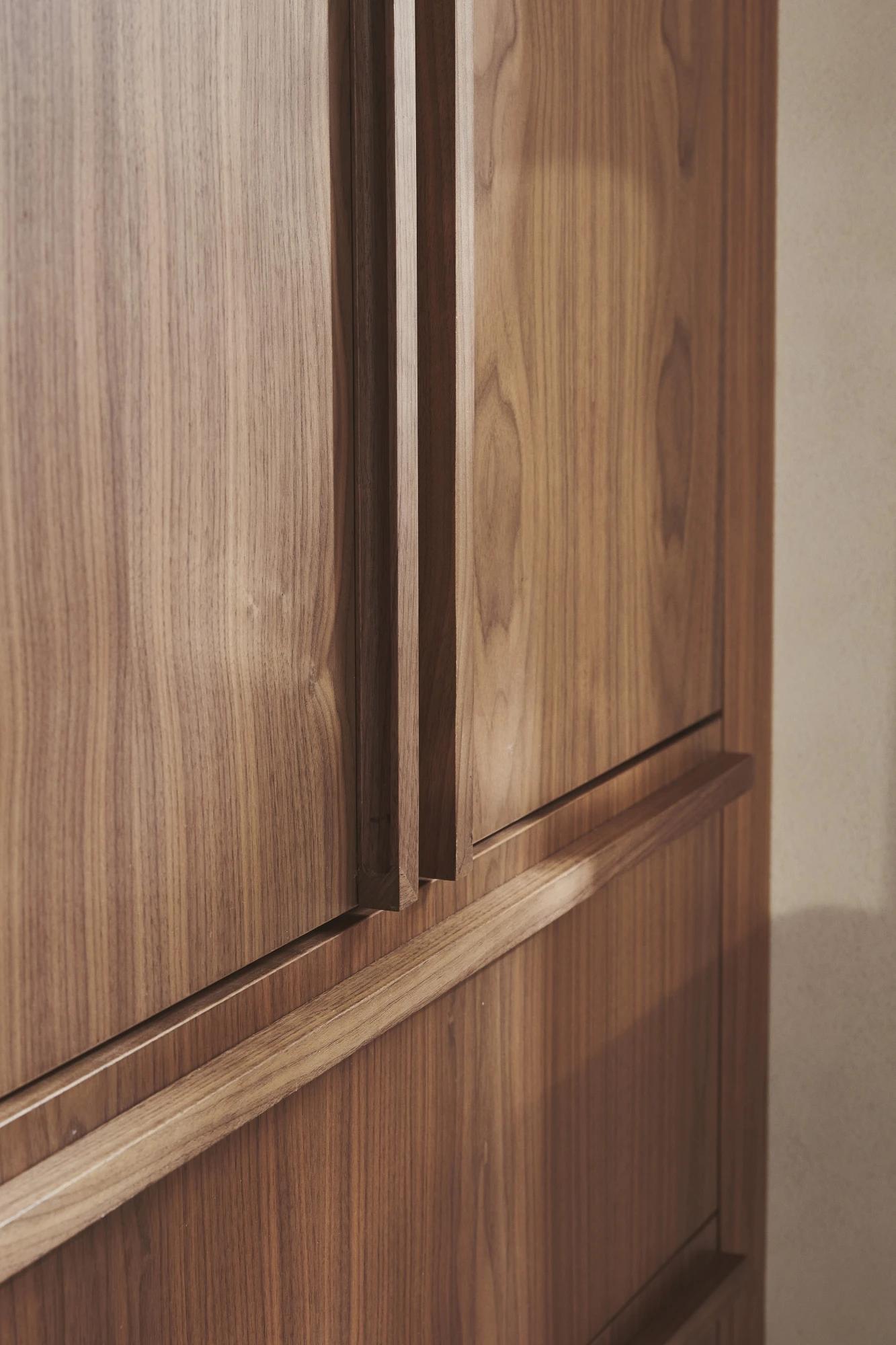 Close-up of a wooden cabinet with a smooth finish, showing a section of its doors and handles. The wood has a distinct grain pattern with warm, natural tones.