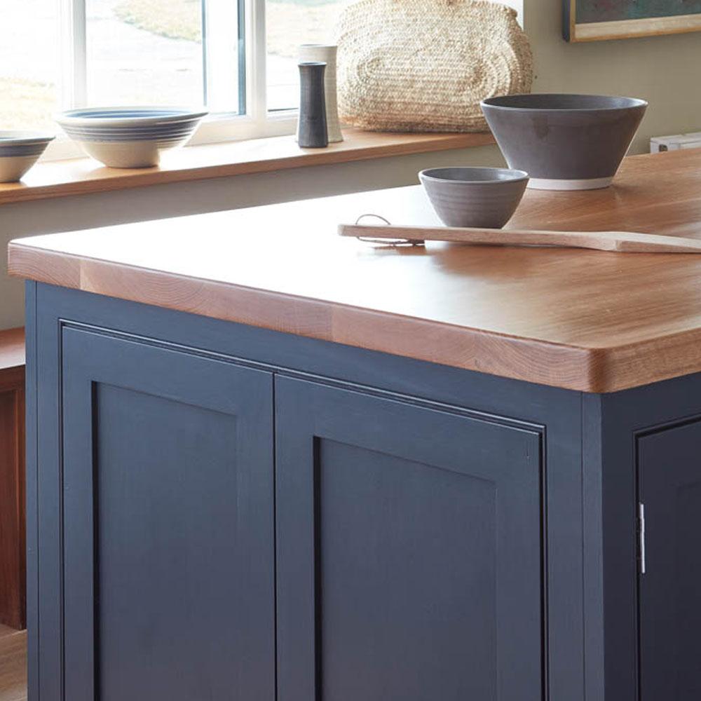 A modern kitchen island with dark blue cabinets and a wooden countertop, topped with ceramic bowls and a wooden spoon; additional bowls are displayed on the windowsill behind.