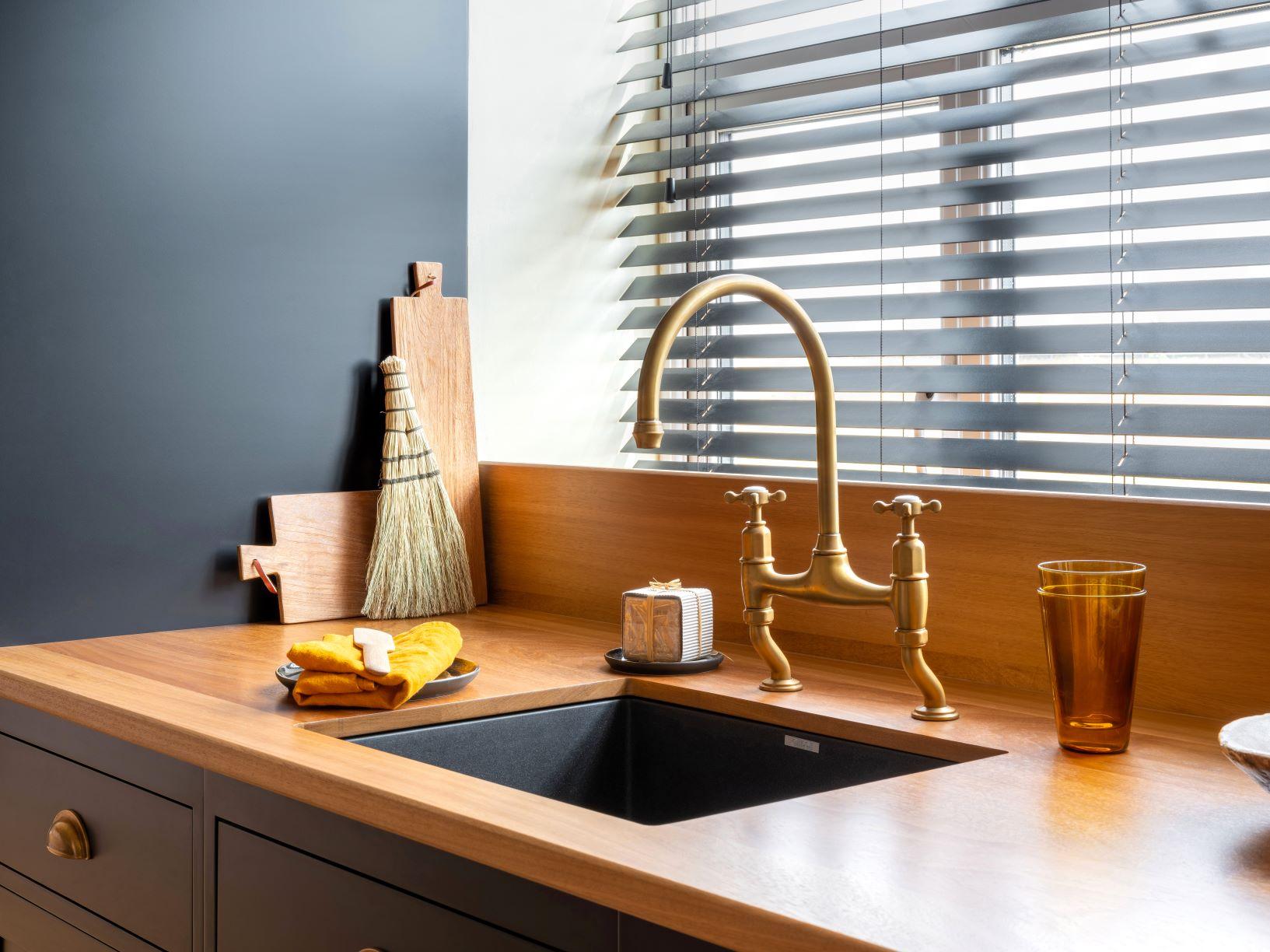An elegant kitchen sink area featuring a brass gooseneck faucet, an undermount black sink, and a warm wooden countertop next to a dark gray accent wall.