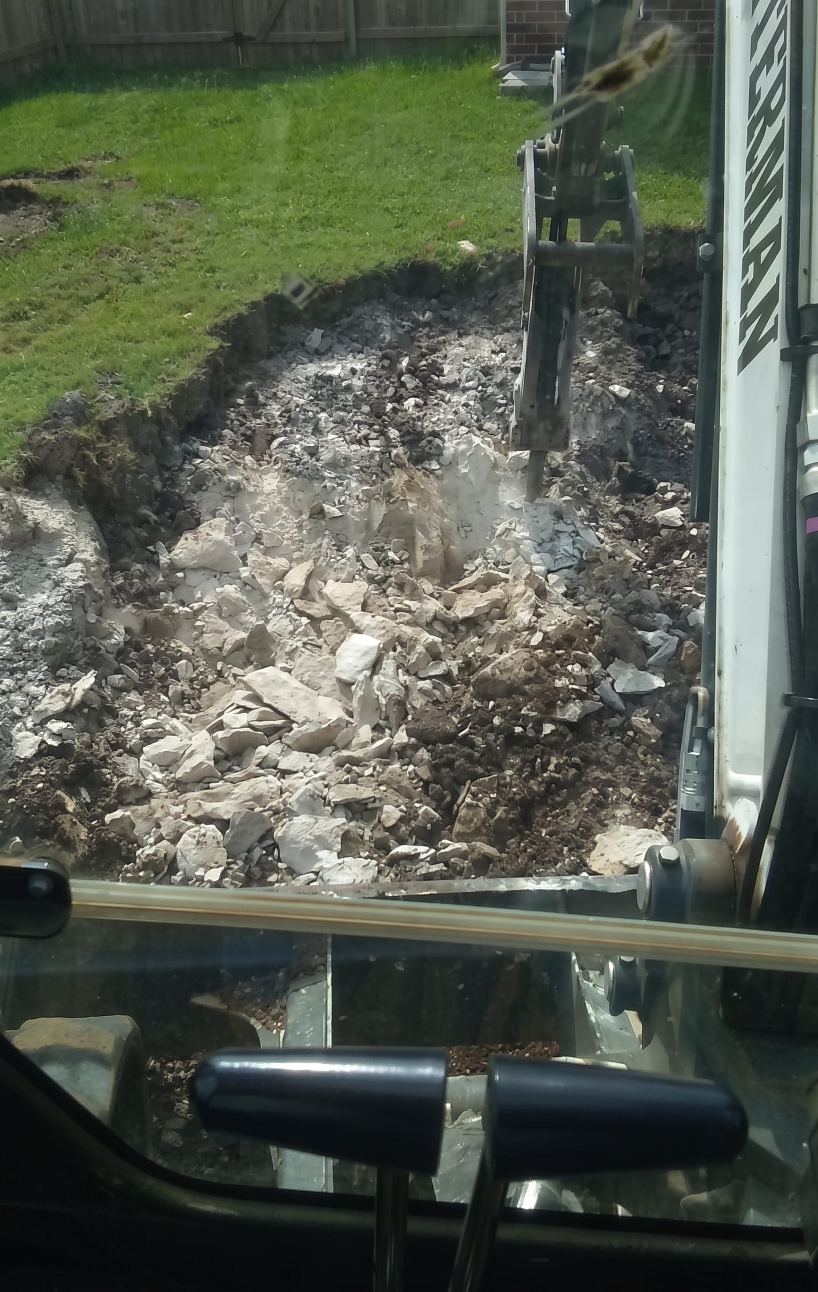 An excavator tearing out a burned structure, seen from the cab