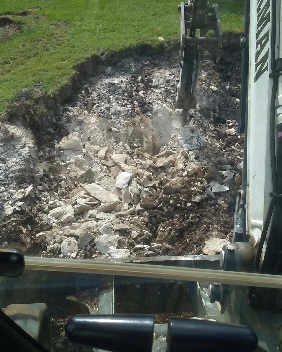 An excavator tearing out a burned structure, seen from the cab