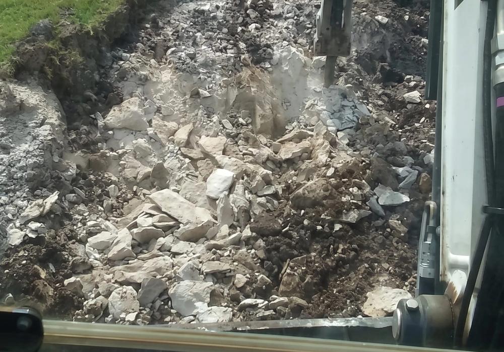 An excavator tearing out a burned structure, seen from the cab