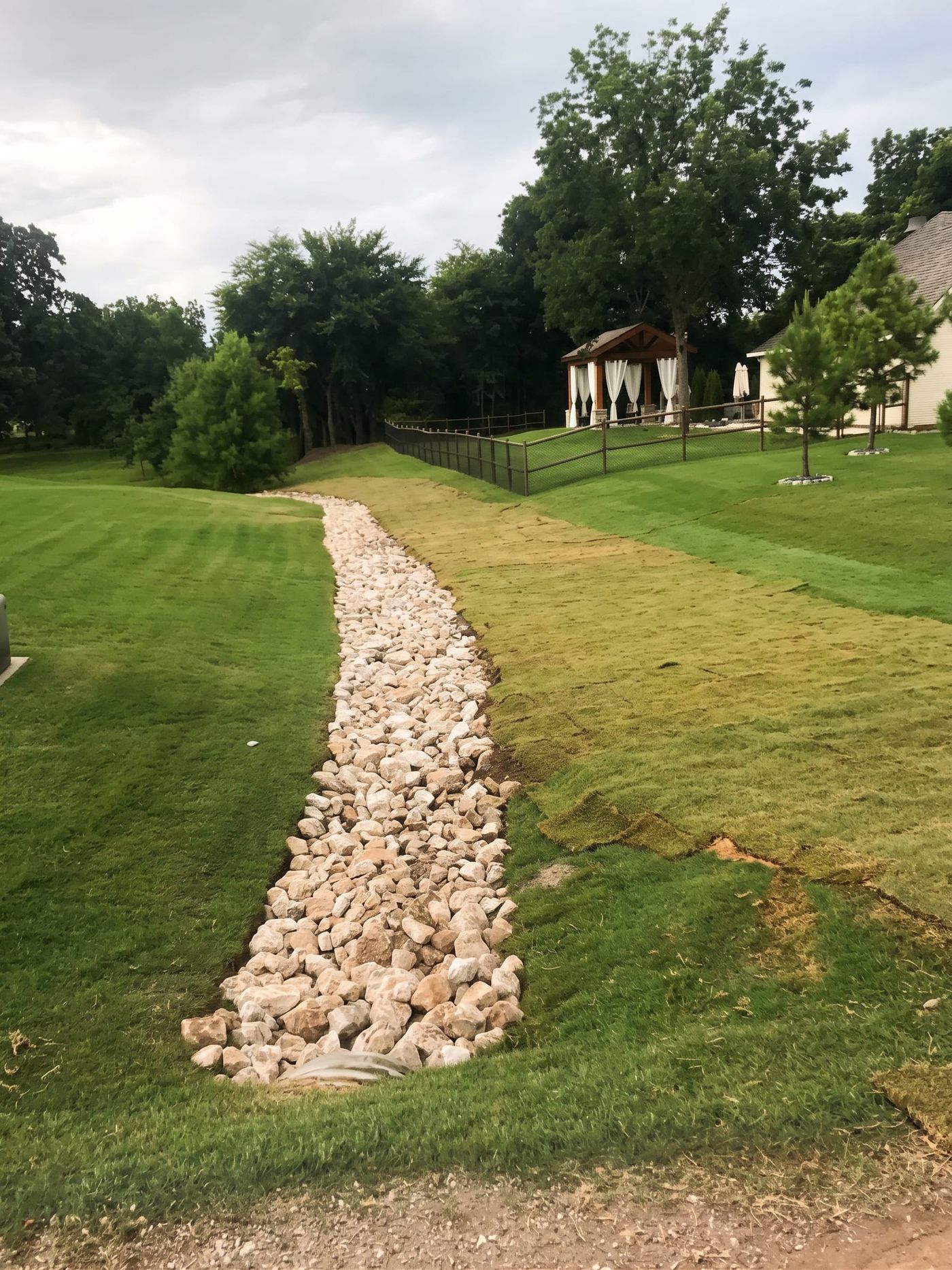 A rock-lined drainage swale through a lawn