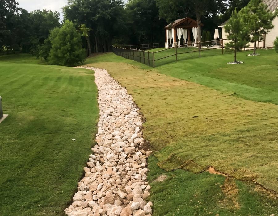A rock-lined drainage swale through a lawn