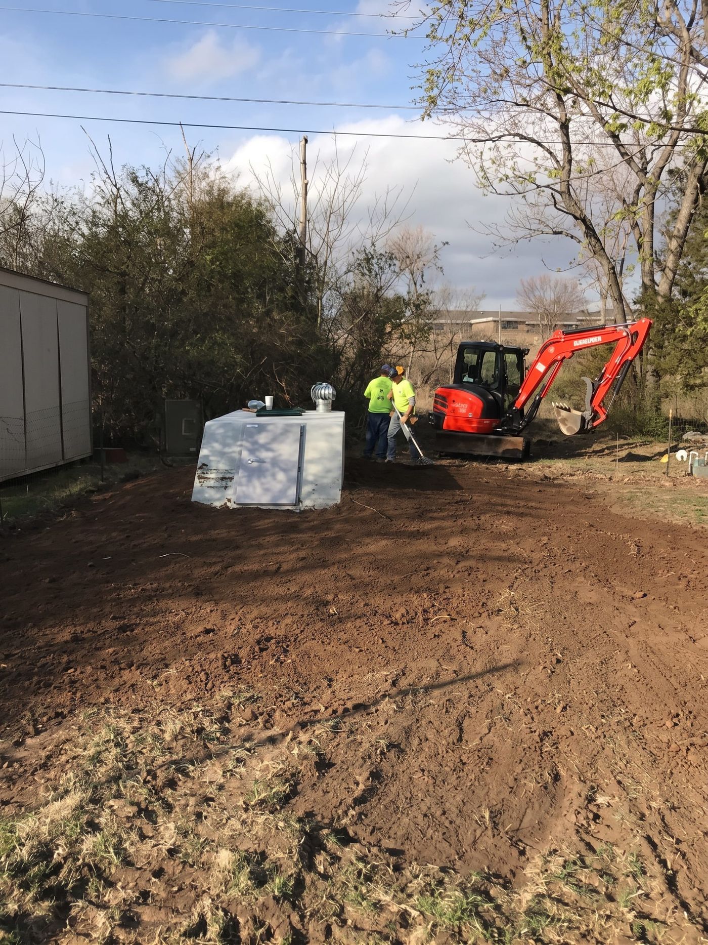 An excavator setting a storm shelter in a back yard