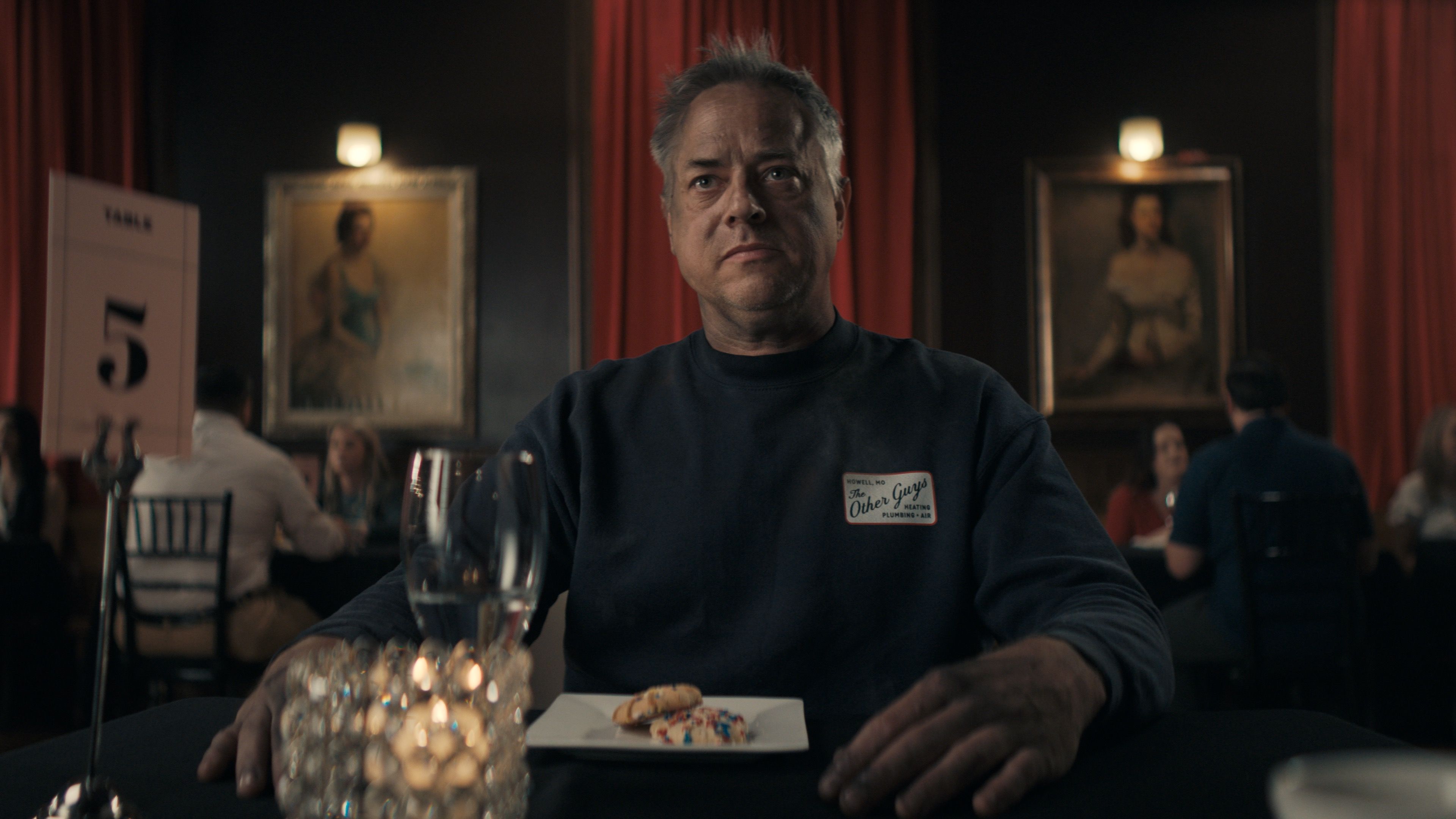 actor sitting at a table in a commercial scene