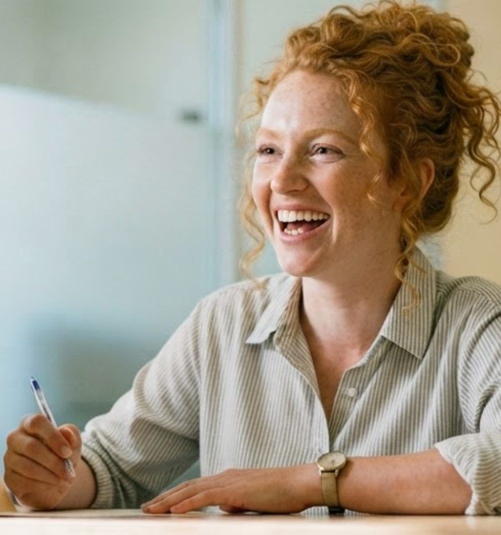 A staff member laughing at a desk, pen in hand