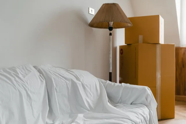 Afgedekte zetel en ingepakte verhuisdozen in een lichte kamer