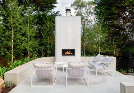 White modern outdoor fireplace with architectural concrete curved bench seating in a treelined setting