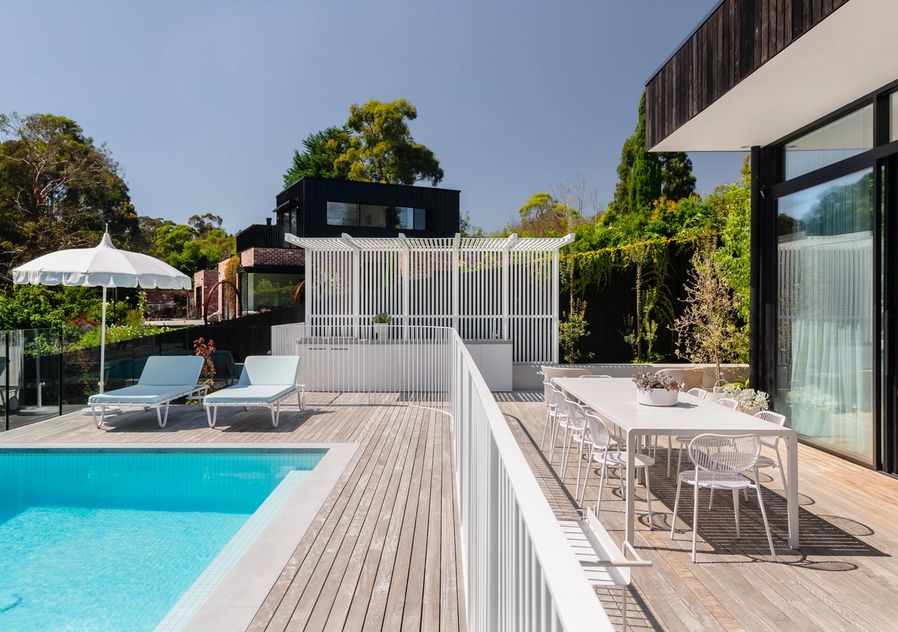 Image showing the poolside decking up to the end where a dining setting and outdoor kitchen is featured