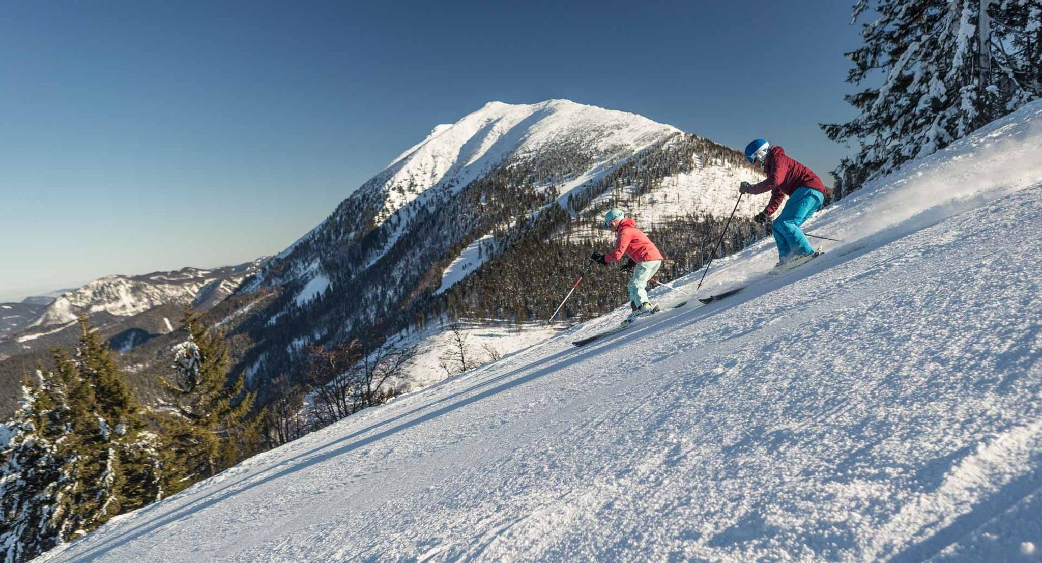 Zwei Skifahrer fahren eine Piste steil bergab