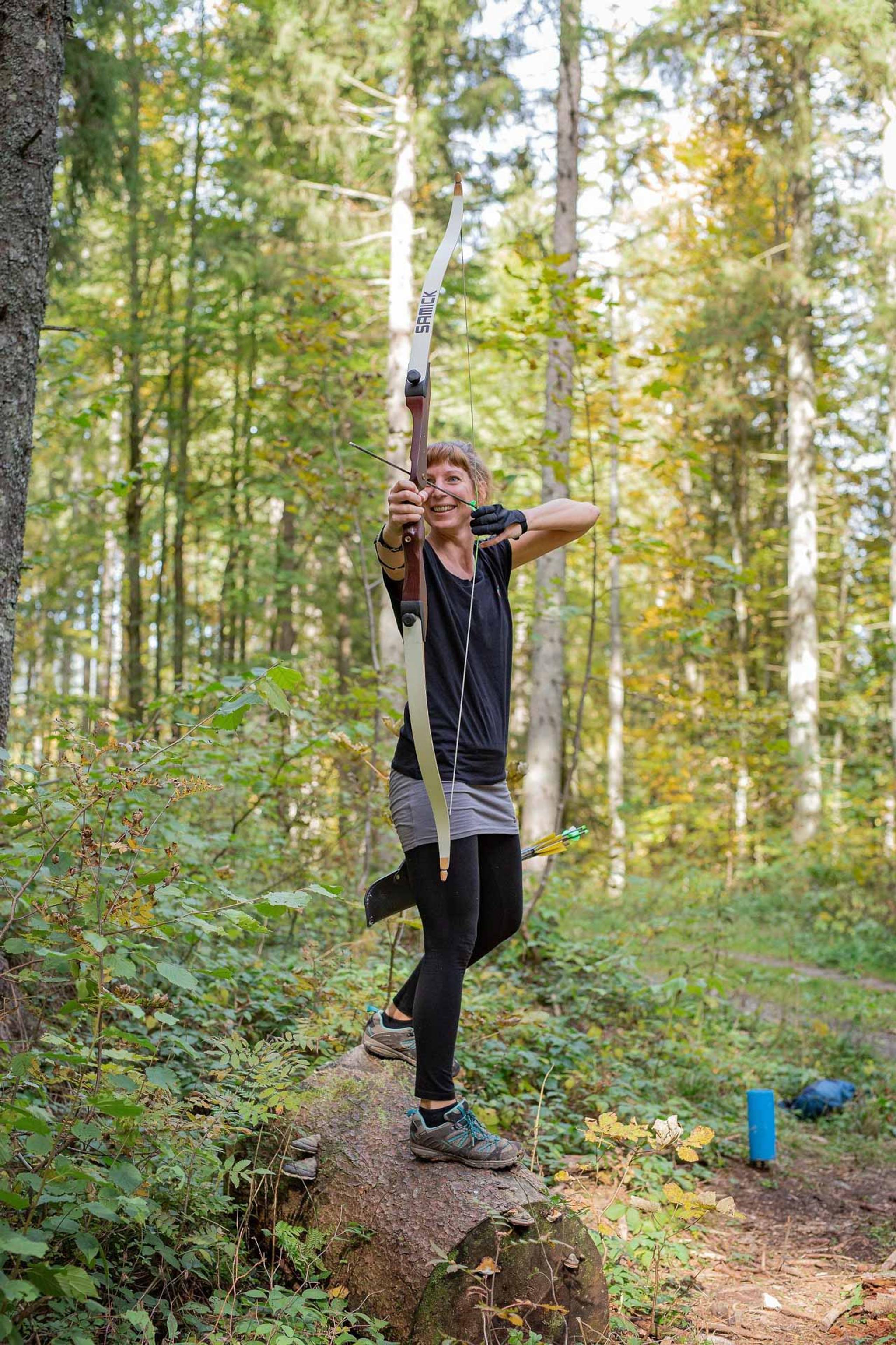 Eine Frau steht im 3D Bogenparkour-Wald und zielt mit Pfeil und Bogen