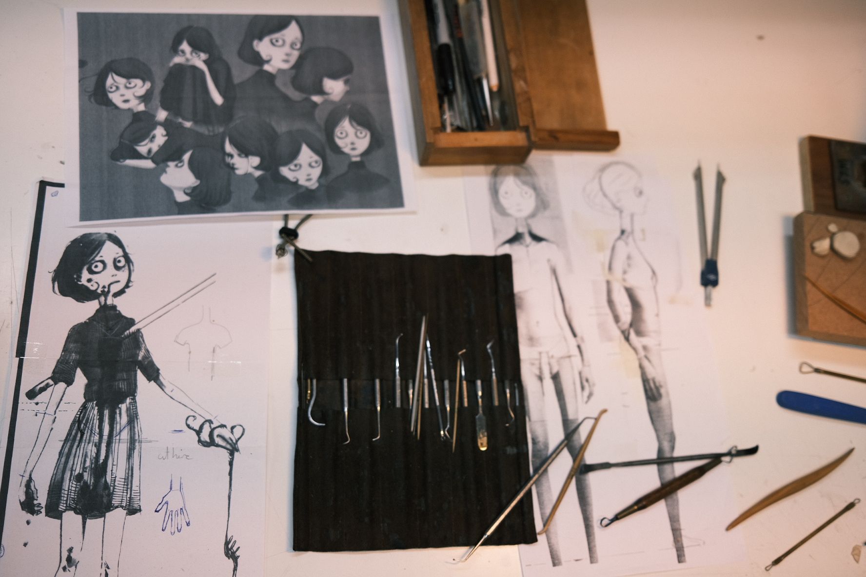 Character sketches and reference art surround sculpting tools arranged on a white worktable.