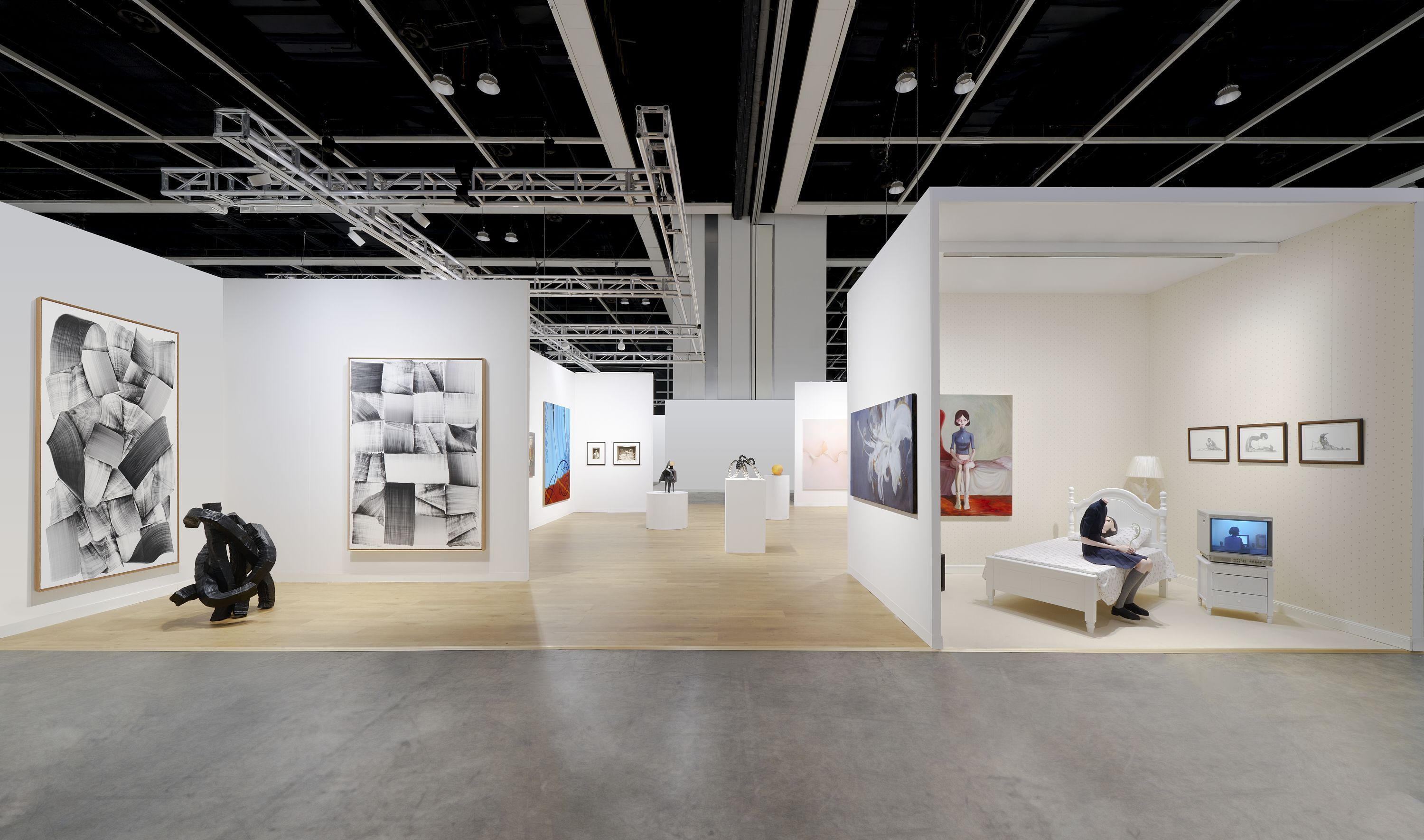 Contemporary art gallery with abstract works, sculptures, and a bedroom installation featuring a seated figure