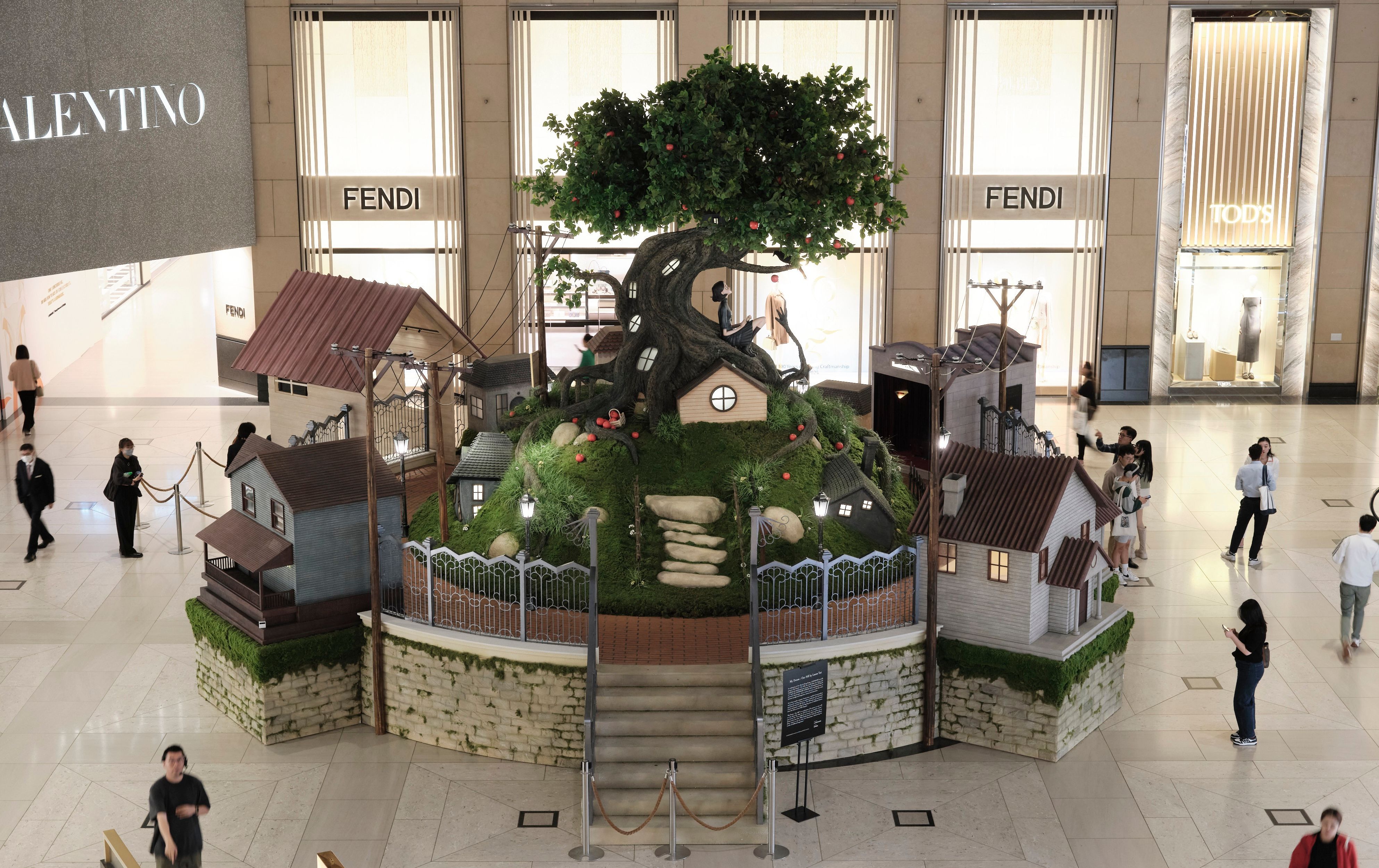 Whimsical miniature village built around a giant fruit-bearing tree in a luxury shopping mall.