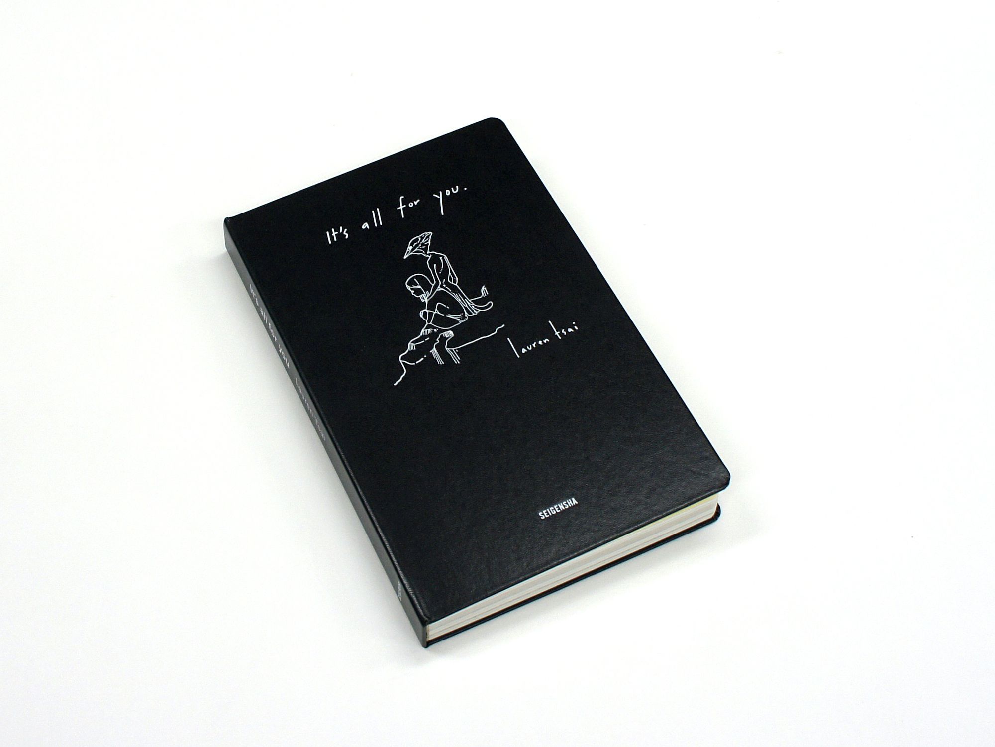 Black hardcover book with white line art and handwritten text, resting diagonally on a white surface.