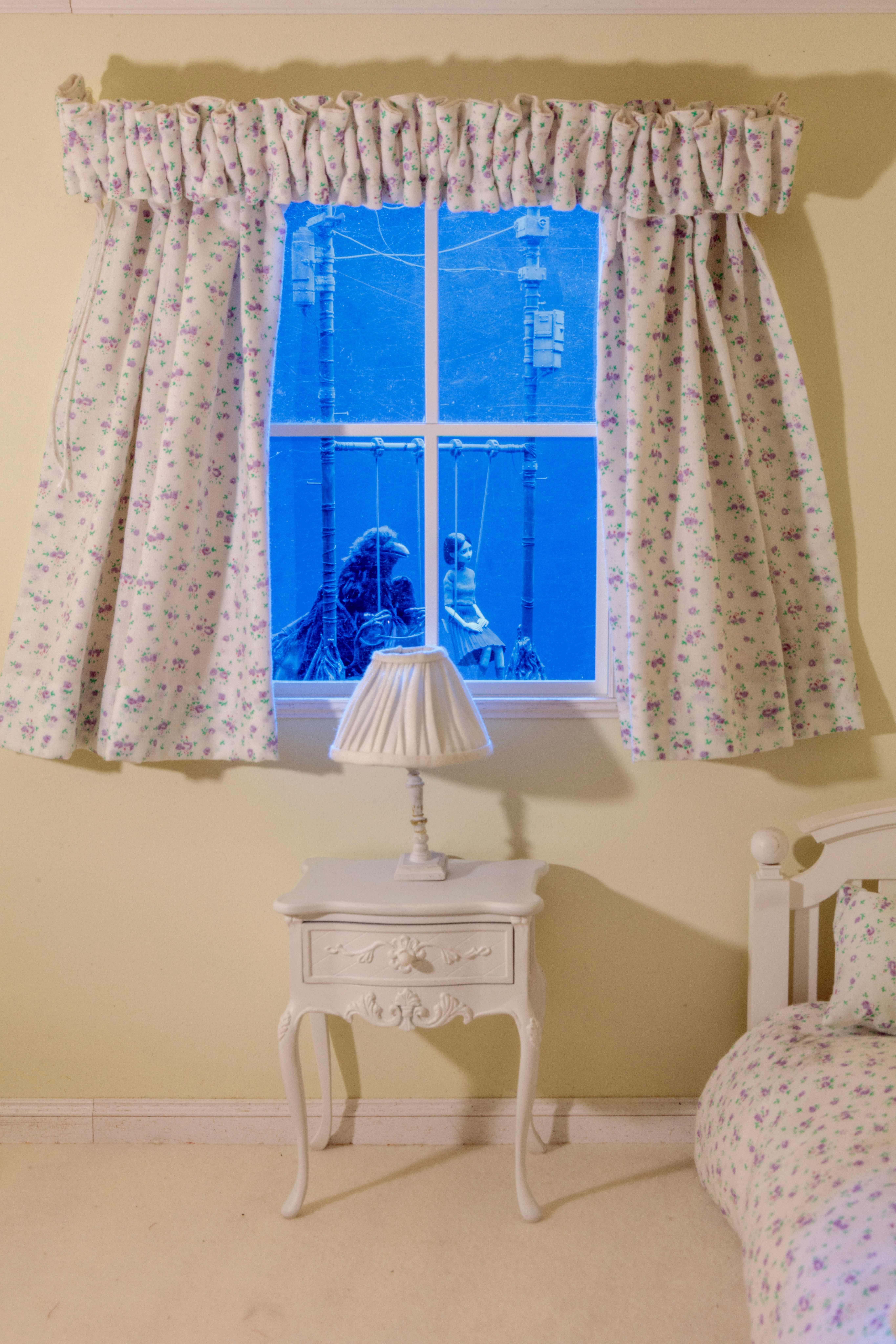 Floral-curtained bedroom window reveals two eerie figures on swings in blue light outside.