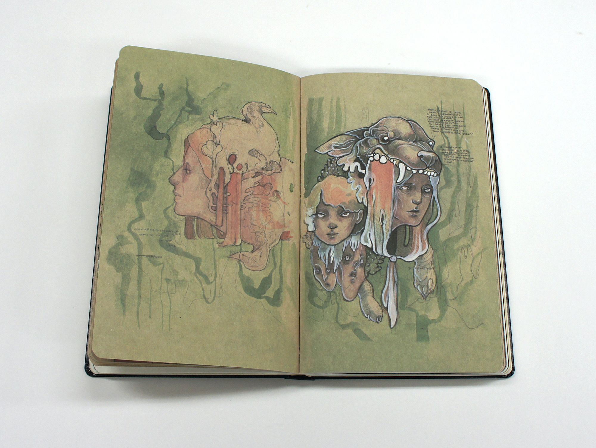 Open sketchbook with surreal mixed-media portraits, including faces beneath a fanged animal headdress.