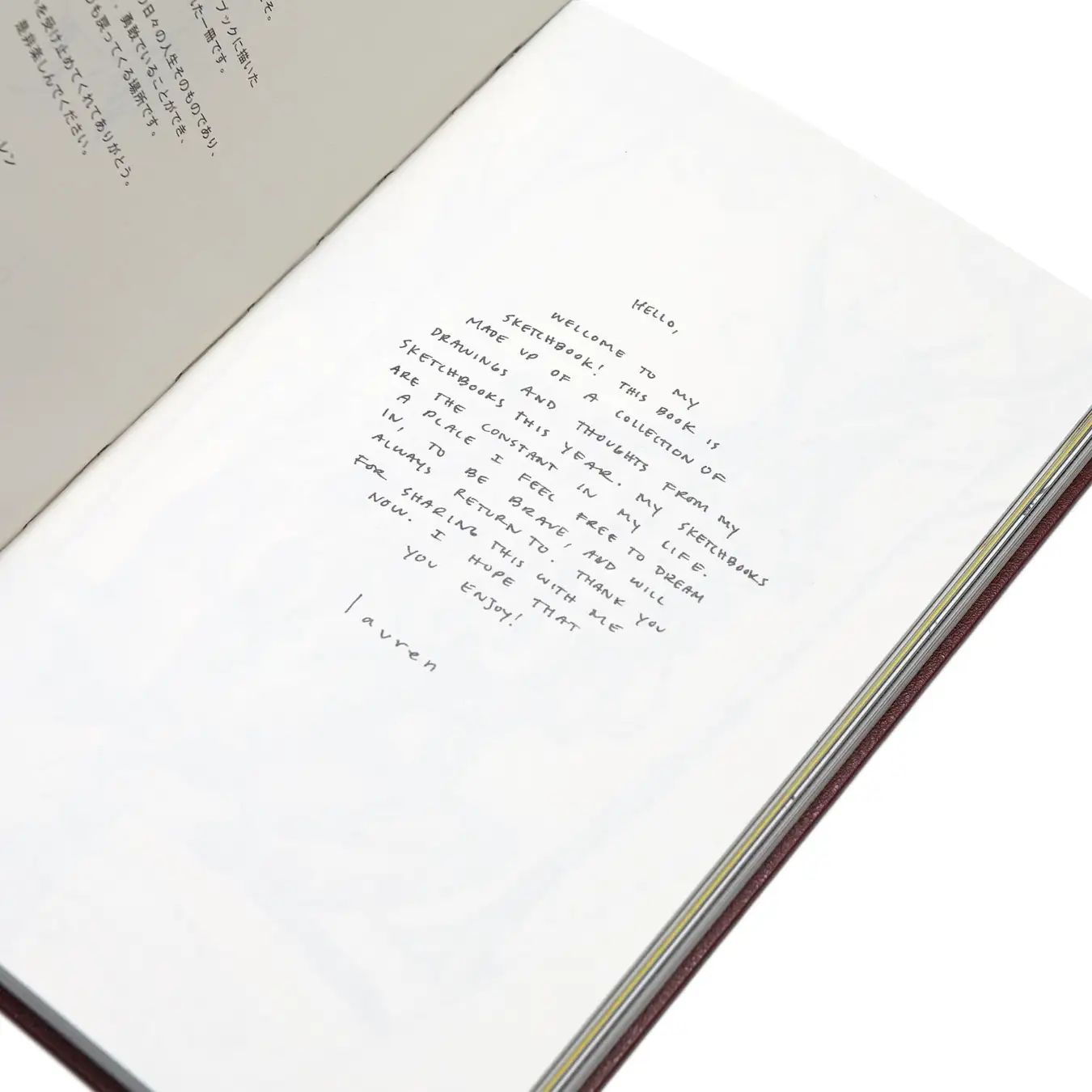 Open sketchbook with a handwritten English introduction and signature, beside a page of Japanese text.