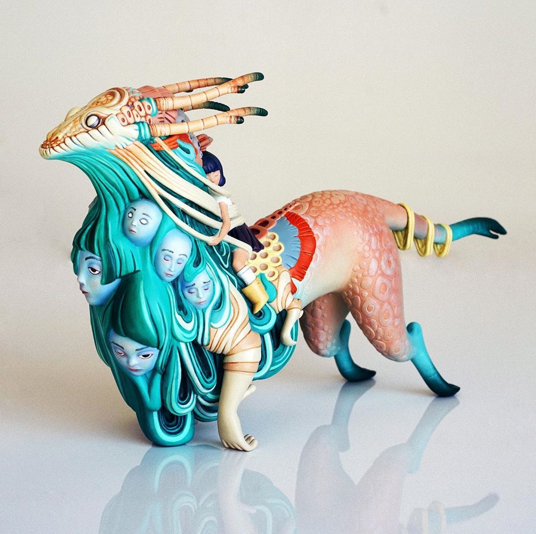 Surreal sculpture of a child riding a colorful horned creature draped in turquoise hair and human faces