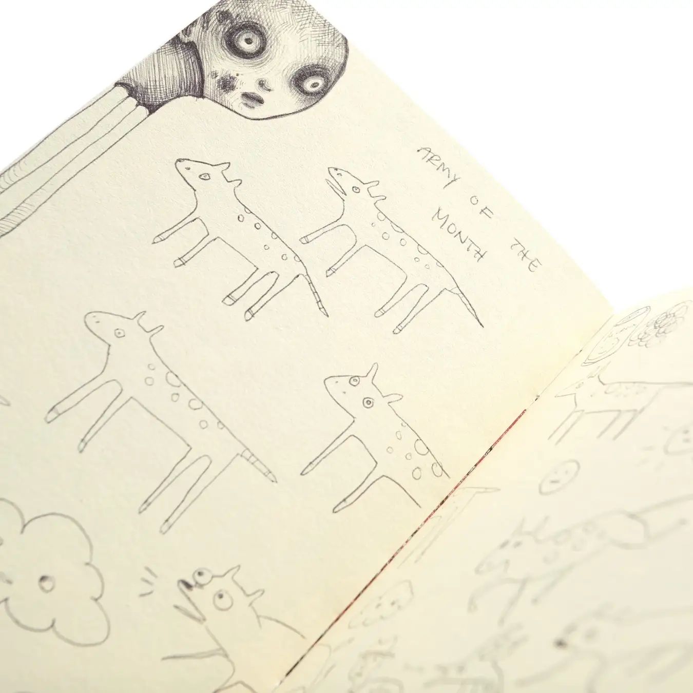 Open sketchbook page with pencil drawings of spotted, horned creatures and a large wide-eyed figure peering over it.