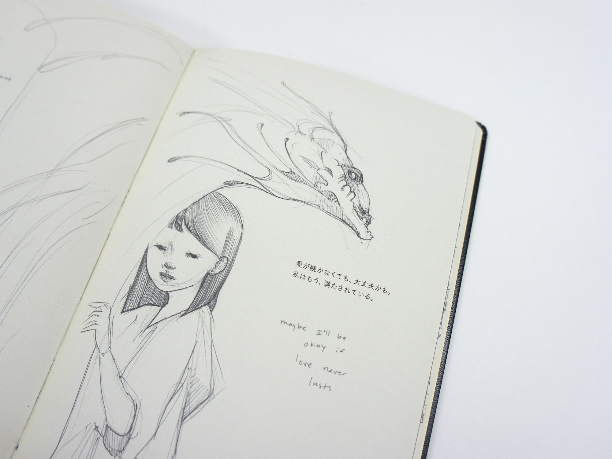 Open sketchbook with pencil drawings of a long-haired woman and a dragon, alongside Japanese and English text.